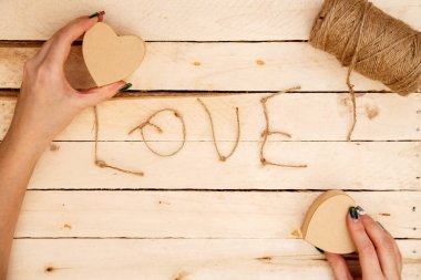 women's hands spread hearts and the word love of threads on a light wooden background. the view from the top