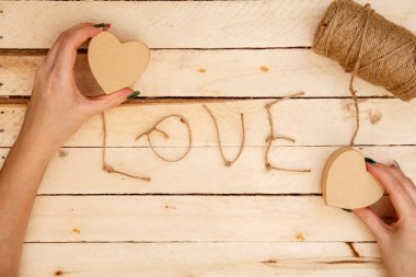 women's hands spread hearts and the word love of threads on a light wooden background. the view from the top
