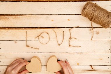 women's hands spread hearts and the word love of threads on a light wooden background. the view from the top