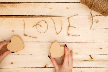 women's hands spread hearts and the word love of threads on a light wooden background. the view from the top