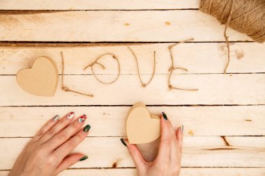 women's hands spread hearts and the word love of threads on a light wooden background. the view from the top