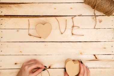 women's hands spread hearts and the word love of threads on a light wooden background. the view from the top