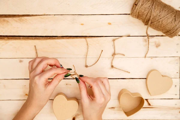 women's hands spread hearts and the word love of threads on a light wooden background. the view from the top