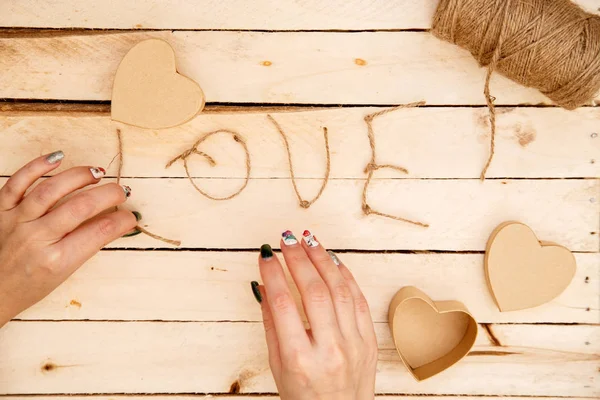women's hands spread hearts and the word love of threads on a light wooden background. the view from the top