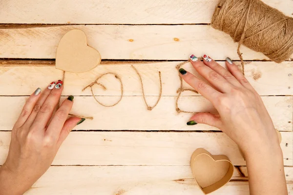 women's hands spread hearts and the word love of threads on a light wooden background. the view from the top