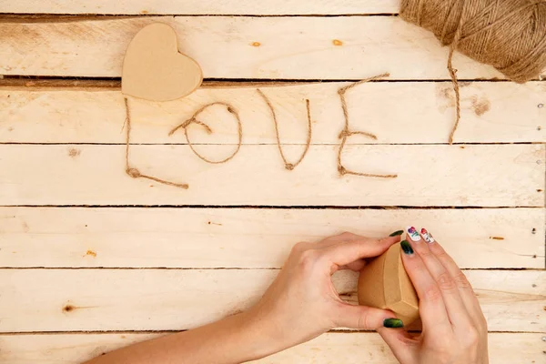 women's hands spread hearts and the word love of threads on a light wooden background. the view from the top