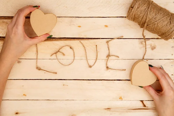 women's hands spread hearts and the word love of threads on a light wooden background. the view from the top