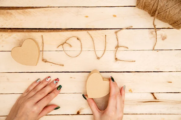 women's hands spread hearts and the word love of threads on a light wooden background. the view from the top