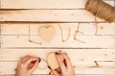 women's hands spread hearts and the word love of threads on a light wooden background. the view from the top