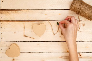 women's hands spread hearts and the word love of threads on a light wooden background. the view from the top