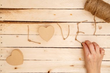 women's hands spread hearts and the word love of threads on a light wooden background. the view from the top