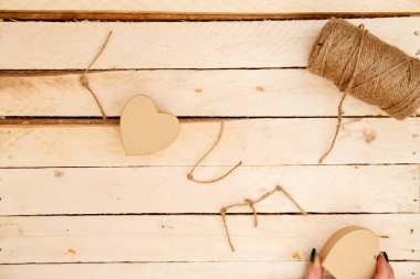 women's hands spread hearts and the word love of threads on a light wooden background. the view from the top