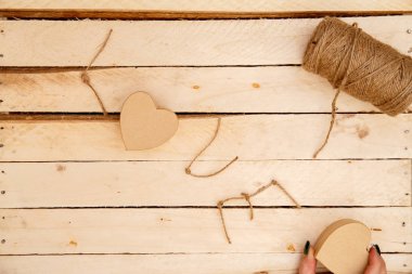 women's hands spread hearts and the word love of threads on a light wooden background. the view from the top