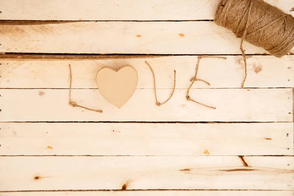 women's hands spread hearts and the word love of threads on a light wooden background. the view from the top