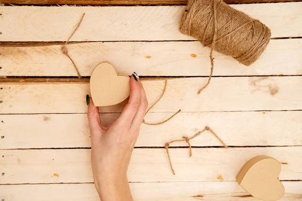 women's hands spread hearts and the word love of threads on a light wooden background. the view from the top