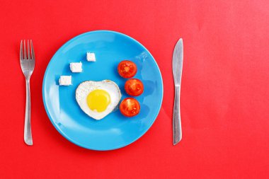 kırmızı bir arka plan üzerinde mavi bir tabak üzerinde kalp şeklinde kızarmış yumurta