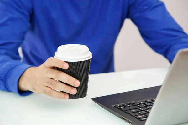 Руки молодого чоловіка, що тримає каву і друкує на ноутбуці — стокове фото