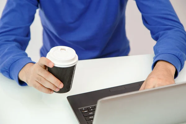 Χέρια ενός νεαρού άντρα που κρατά καφέ και εκτυπώνει σε ένα φορητό υπολογιστή — Φωτογραφία Αρχείου