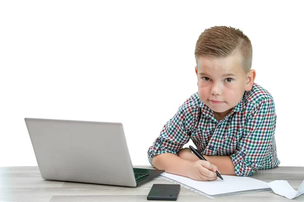 Caucasian school-age boy in a plaid shirt sitting at the table a — Stock Photo, Image