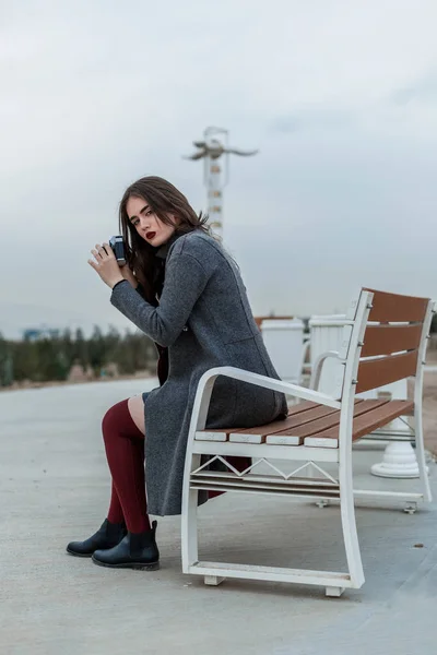 Young beautiful girl in Burgundy stockings and gray coat sitting — 스톡 사진