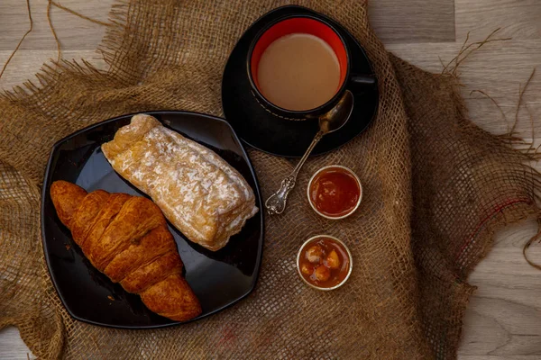 Eclair, puff doce tubo em uma placa preta e uma xícara de café sagacidade — Fotografia de Stock