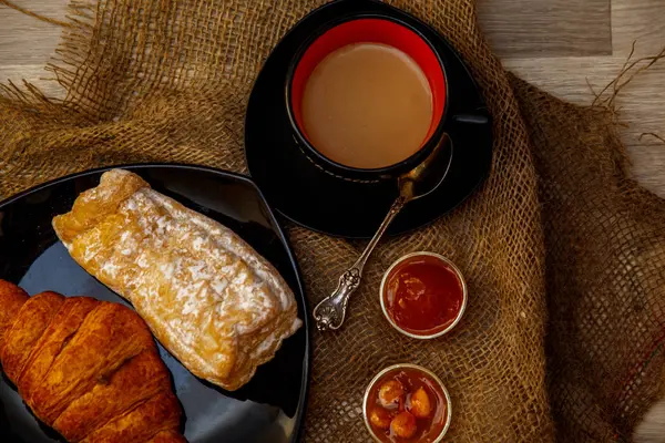 Eclair, puff doce tubo em uma placa preta e uma xícara de café sagacidade — Fotografia de Stock