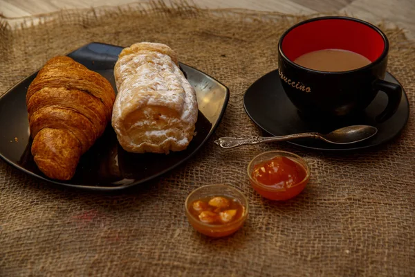 Eclair, soffio dolce tubo su un piatto nero e una tazza di caffè arguzia — Foto Stock