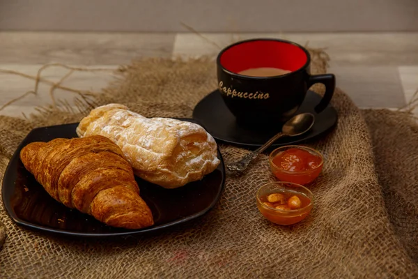 Eclair, puff doce tubo em uma placa preta e uma xícara de café sagacidade — Fotografia de Stock