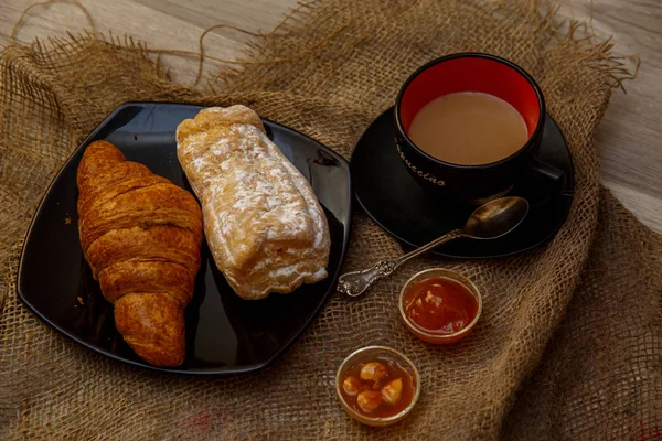 Eclair, puff doce tubo em uma placa preta e uma xícara de café sagacidade — Fotografia de Stock