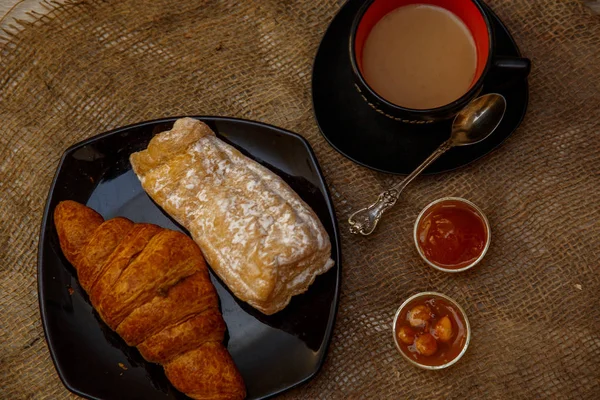 Eclair, puff doce tubo em uma placa preta e uma xícara de café sagacidade — Fotografia de Stock