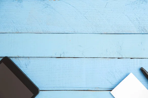 Zwarte Tablet, kleine notebook en zwarte pen op blauwe houten backgr — Stockfoto