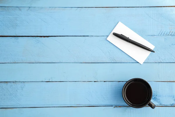 Een kopje drank en een papieren notitieboekje met een zwarte pen op een blauwe w — Stockfoto