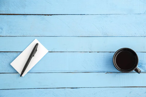 Een kopje drank en een papieren notitieboekje met een zwarte pen op een blauwe w — Stockfoto