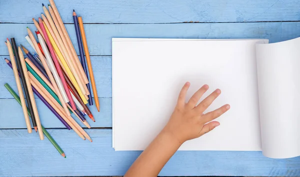 children's hands draw with pencils in the album on the blue tabl