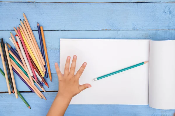 children's hands draw with pencils in the album on the blue tabl