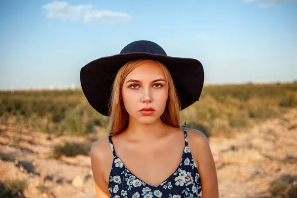 A close-up portrait of a blue-eyed blonde girl in a black hat an — Stock Photo, Image