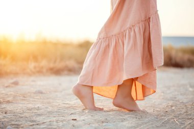 güneşlenme sırasında kum üzerinde yürüyen pembe elbiseli bir kadının ayakları