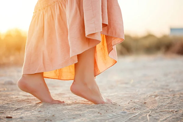 Füße einer Frau im rosafarbenen Kleid, die bei Sonnenuntergang im Sand spaziert — Stockfoto