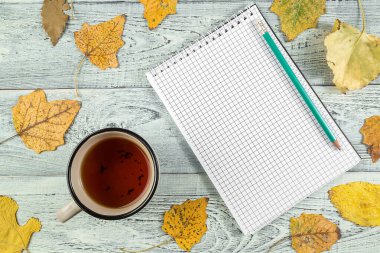 Sarı sonbahar yaprakları, bir fincan çay ve hafif eski bir defter.