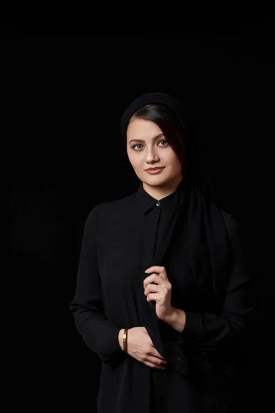 a young beautiful Muslim woman with brown hair in a black blouse and black leather skirt on a black isolated background