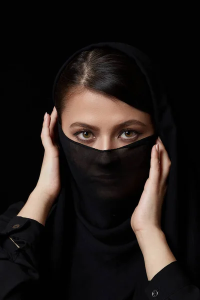若い美しい暗い髪のイスラム教徒の女性の肖像画彼女の顔は黒の孤立した背景に覆われて — ストック写真
