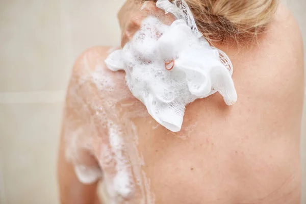 an elderly 60-year-old woman washes in the shower, Soaps her shoulders, back and body with a washcloth in the home bathroom. selective focus, small focus area.