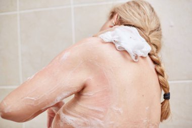 60 yaşında yaşlı bir kadın duşta yıkanıyor ellerini, vücudunu ve göğsünü banyo beziyle sabunluyor. seçici odak, küçük odak alanı.