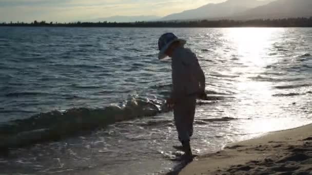 Junge spielt mit Wellen am Strand bei Sonnenuntergang — Stockvideo