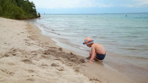 Niño pequeño está jugando en la playa en la arena, junto al mar — Vídeos de Stock