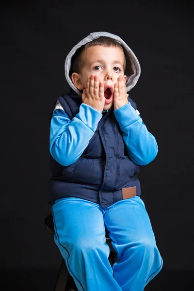 Porträtt Förvånad Liten Pojke Sitter Svart Avföring Isolerad Svart Bakgrund — Stockfoto