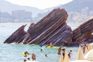 Karadağ, Budva - 12 Temmuz 2018: İnsanlar denizden yapışmasını keskin taş plajda yüzmek