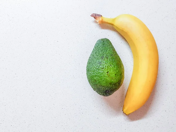 Ripe yellow banana and avocado on the white marble table. Top view