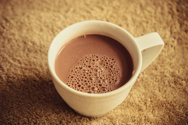 Drink cocoa with bubbles in a white mug on a brown cloth. View from above.