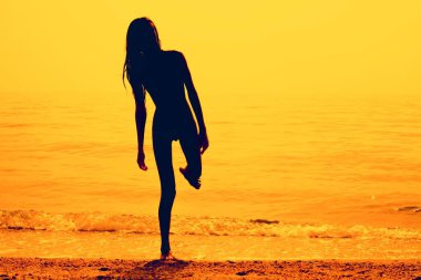 Silhouette of a slim young girl walking along the beach, pink tone. clipart